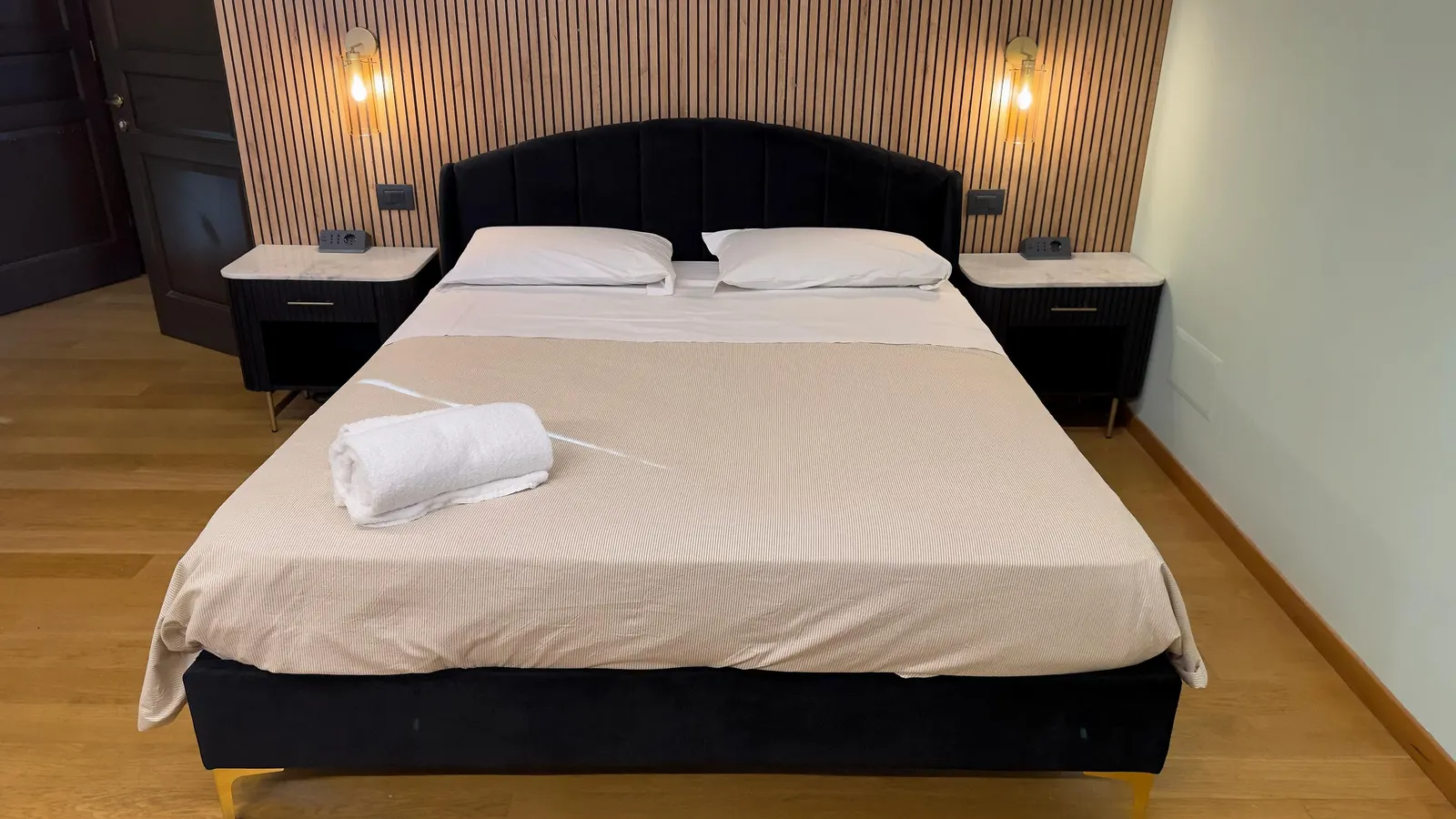 Camera matrimoniale con letto in velluto nero, boiserie in legno e luci in ottone