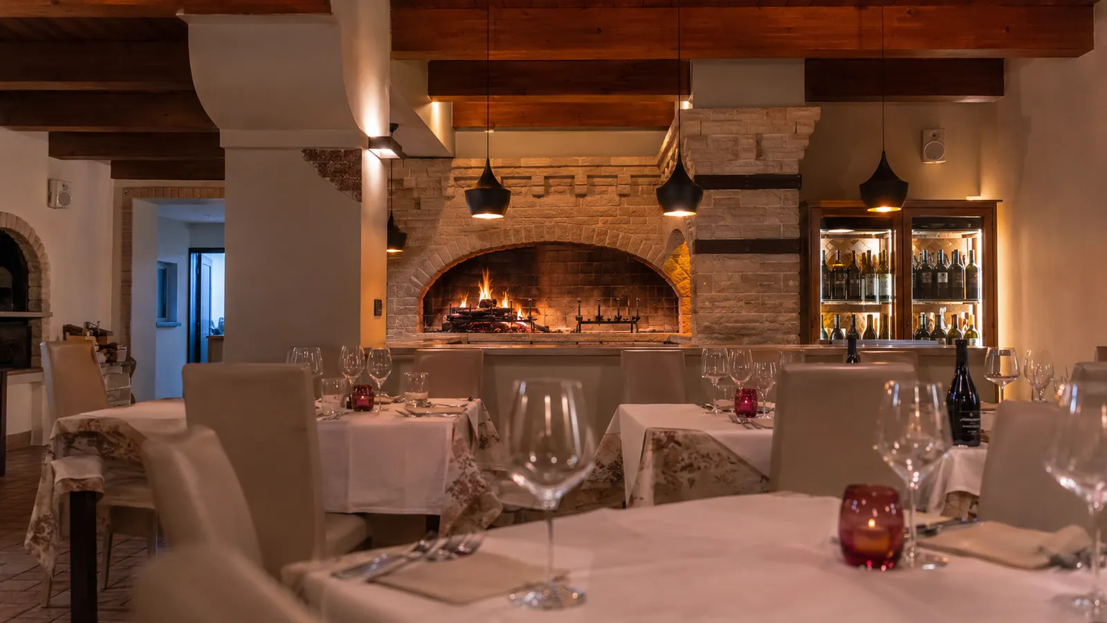 Il camino in pietra della sala con la cantina dei vini illuminata
