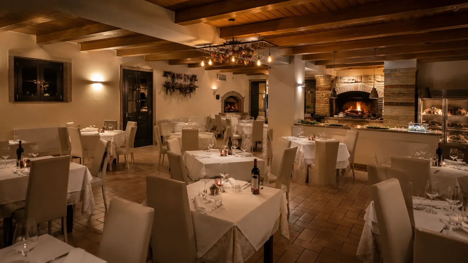 La sala interna del ristorante con tavoli bianchi, travi in legno e camino acceso