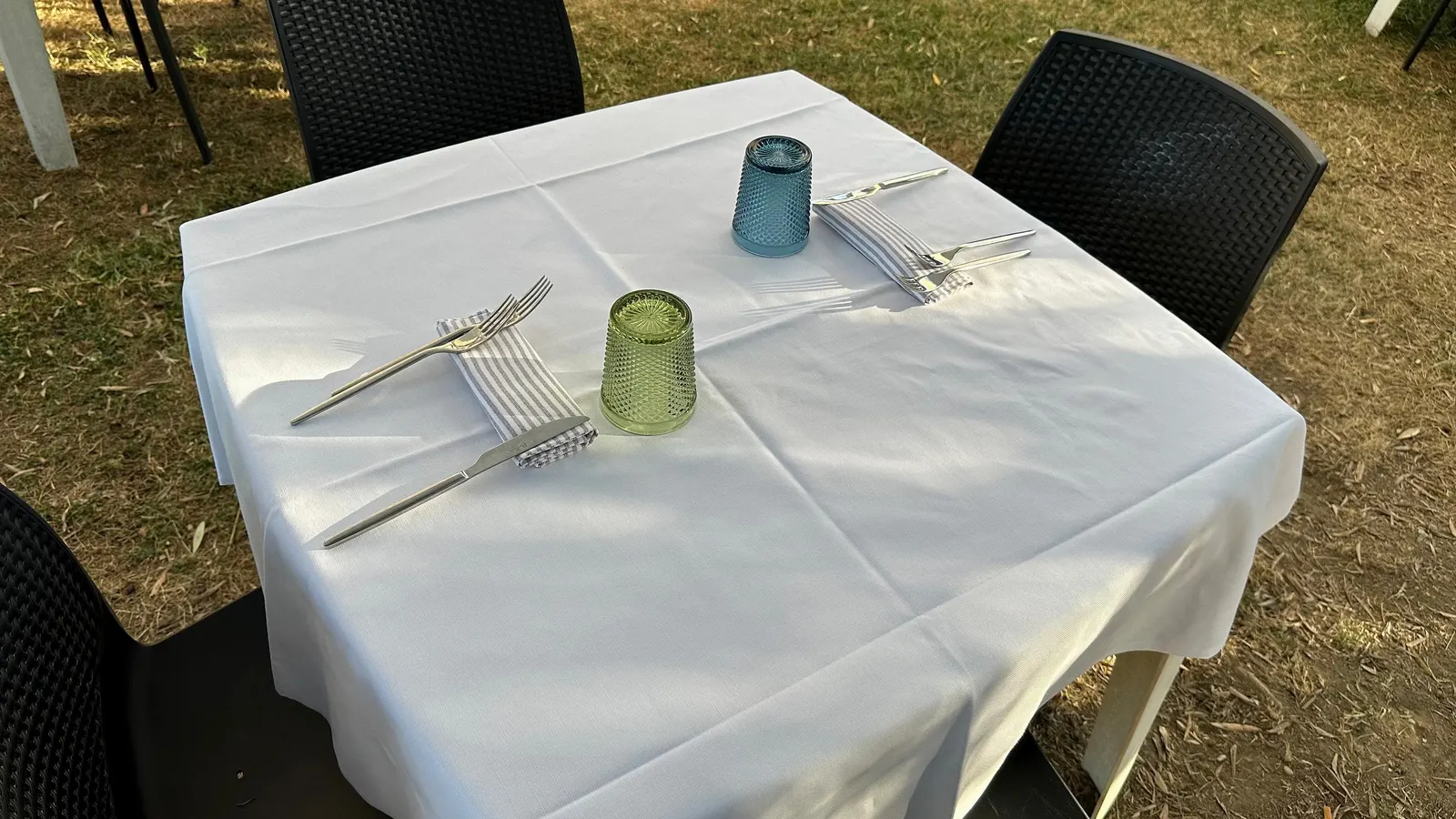 Tavolo con tovaglia bianca, bicchieri colorati e posate all'aperto